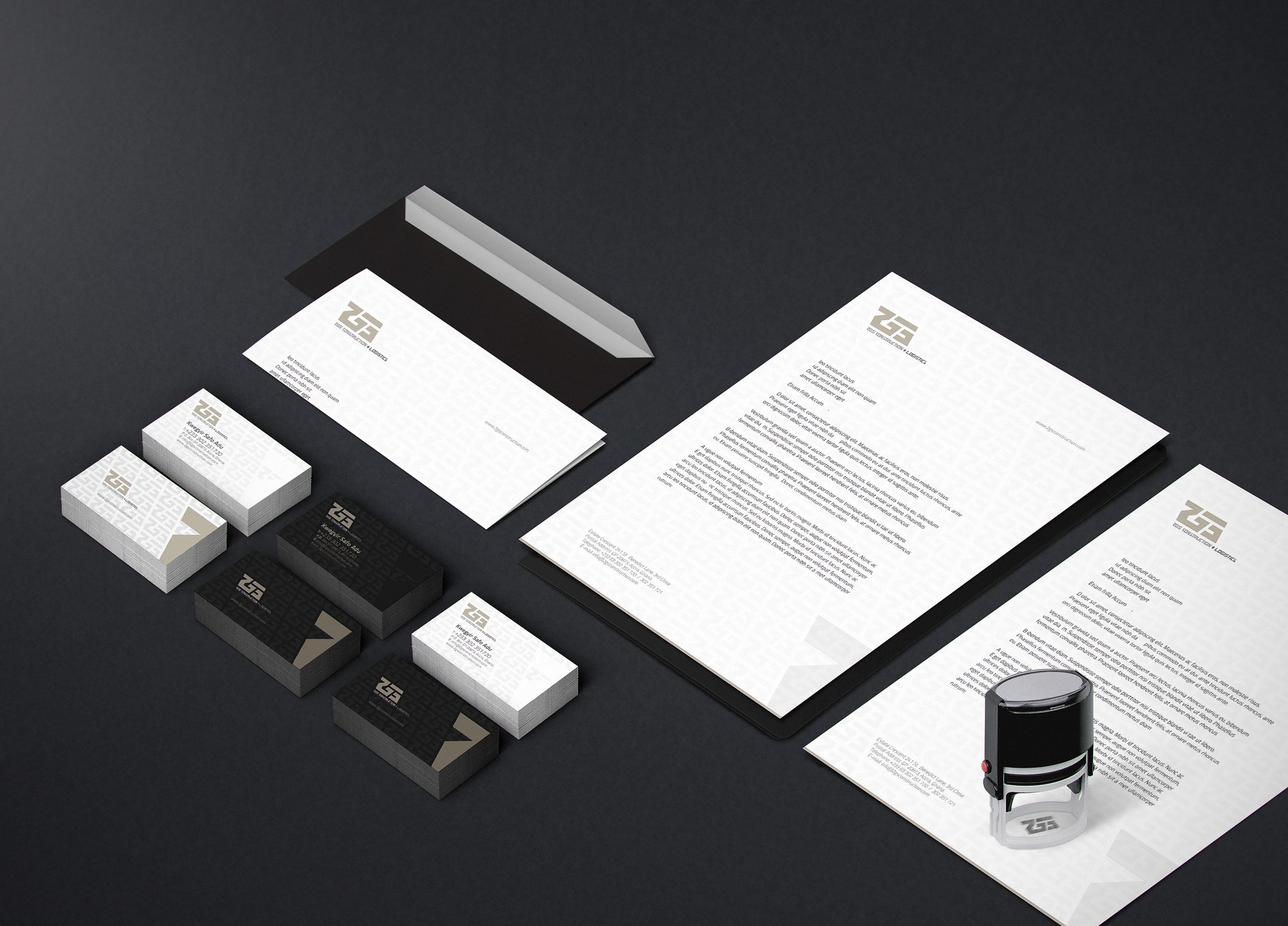 Option one of the stationery suite mocked up on a charcoal ground: the monogram over a single-line 2GS CONSTRUCTION + LOGISTICS lockup, on envelope, letterheads, white and black maze-patterned card stacks and a self-inking stamp