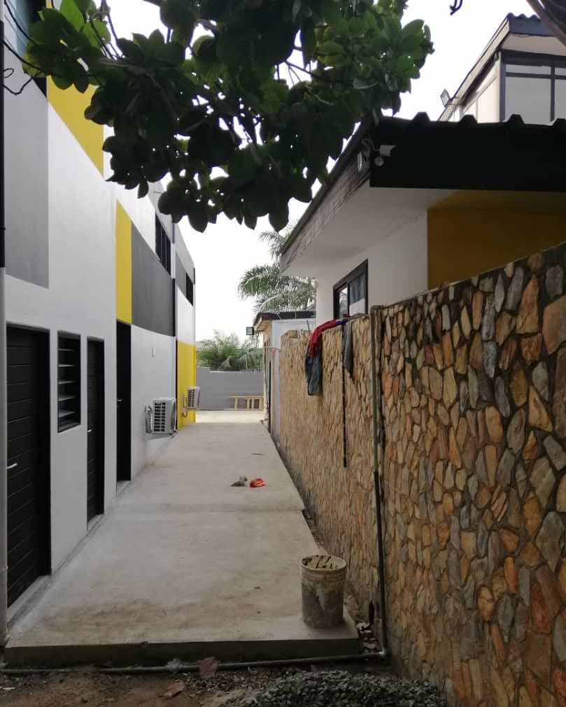 3AAP - the side passage between the building and the stone boundary wall, black doors and louvres banded with yellow and grey