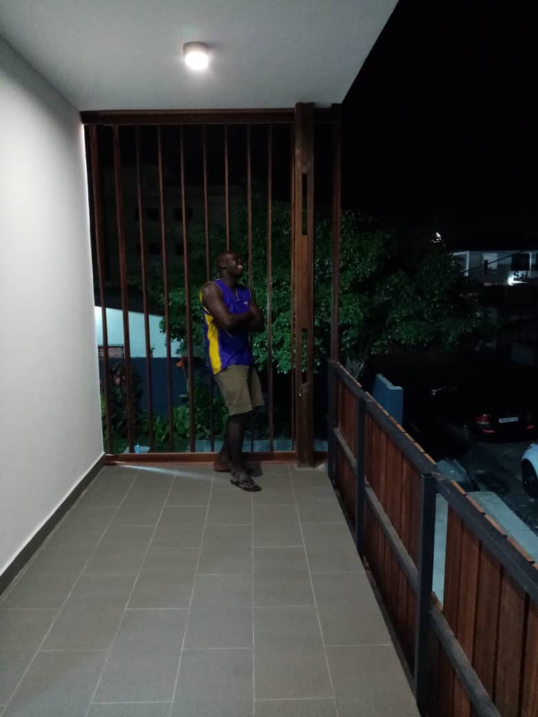 5AAP — the first-floor balcony at dusk: tiling laid, timber balustrade fixed and a worker standing at the screen