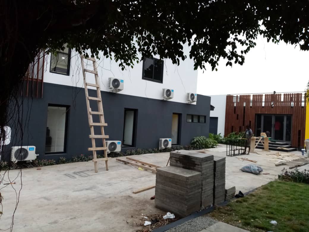 5AAP — the rear elevation with air-conditioning units mounted along the wall, a timber ladder in the yard and stacks of paving slabs waiting to be laid