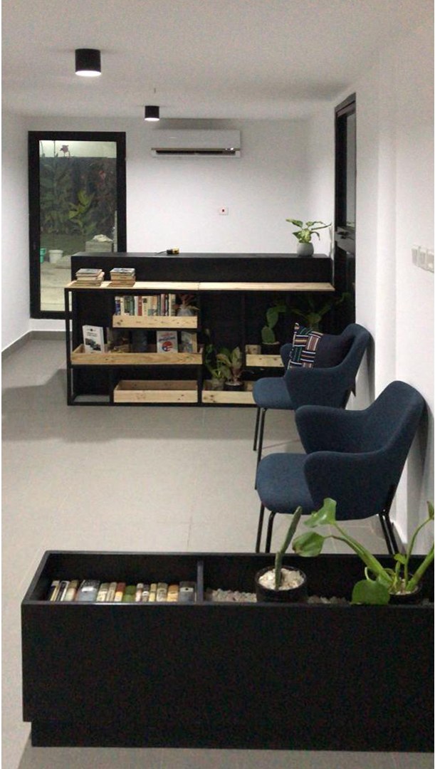 5AAP — the breakout corner: a long black-topped worktable on crate shelving, two navy lounge chairs, and a low planter box laid with books