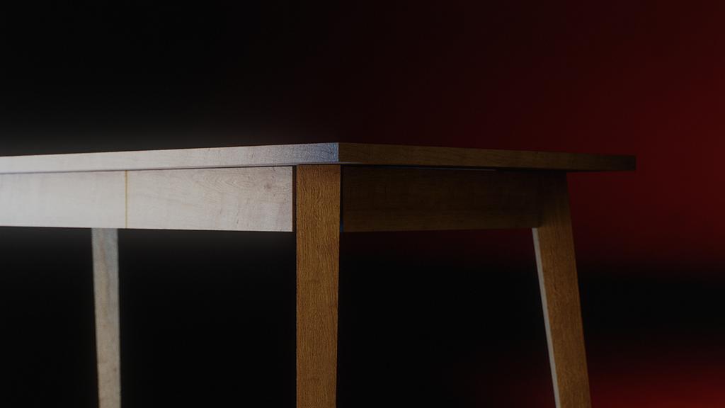 Ackon Desk corner detail: the pale timber top edge meets a darker oak leg and apron against a black backdrop with a red gradient at the right