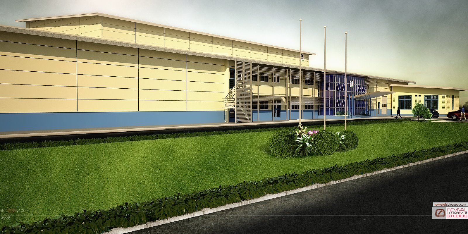The building seen from the road across a sloping lawn: a two-storey cream range on a blue plinth with an external stair and louvre screens, the glazed entrance and its canopy to the right of the block, four bare flagpoles raised from a planted island in the grass, and a hedge-lined kerb along the tarmac in the foreground.