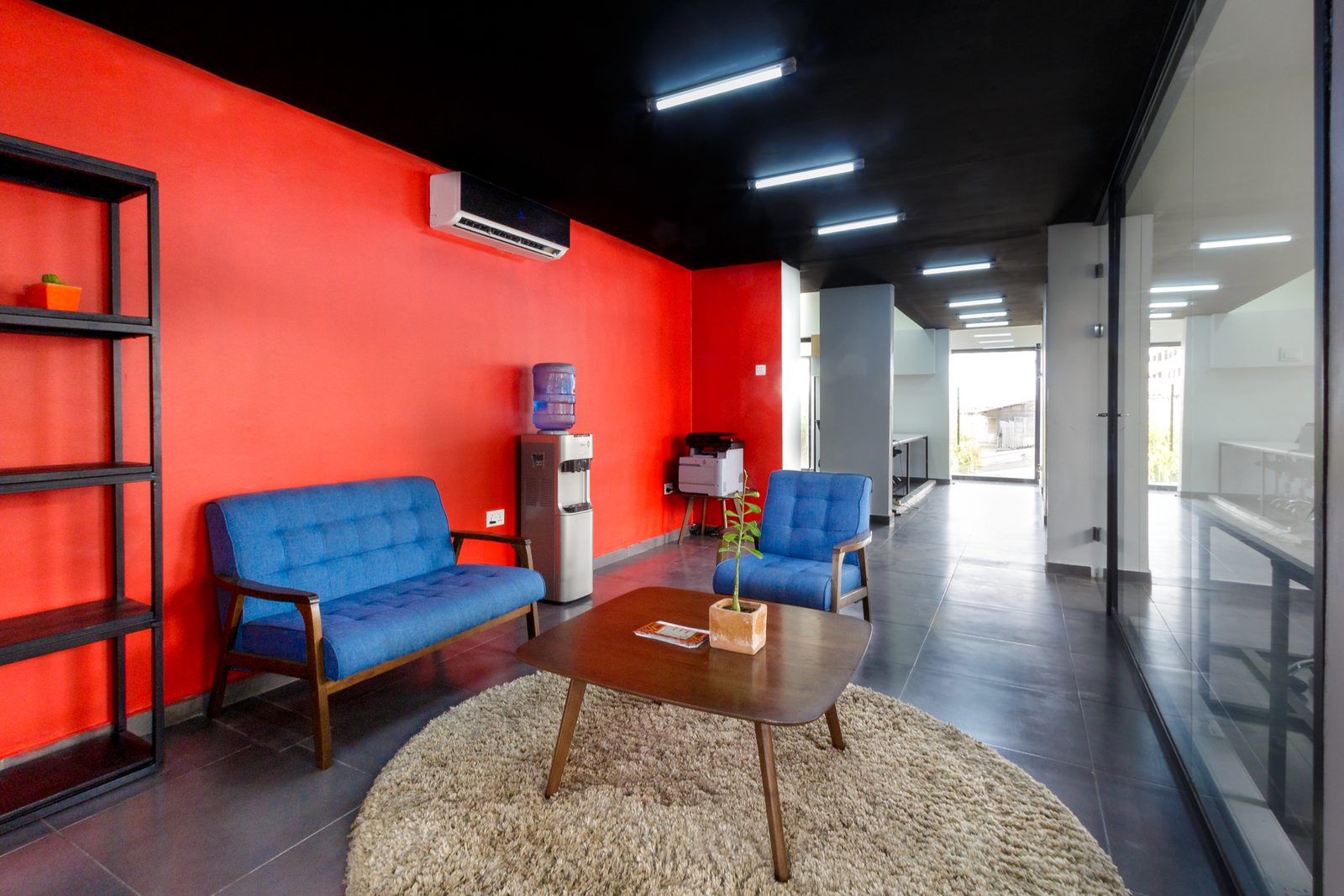 AFG - The full lounge seating group under linear fluorescent battens, red walls either side of the black ceiling and the open plan beyond.