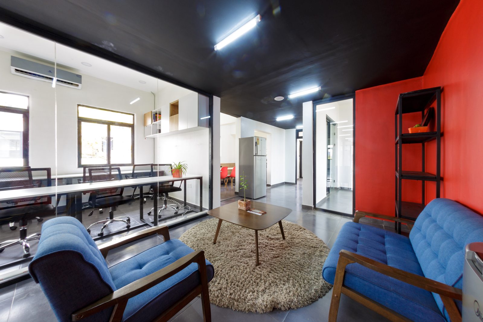 AFG - From the lounge towards the workstations, a blue armchair in the foreground and white-topped bench desks beyond a low partition.