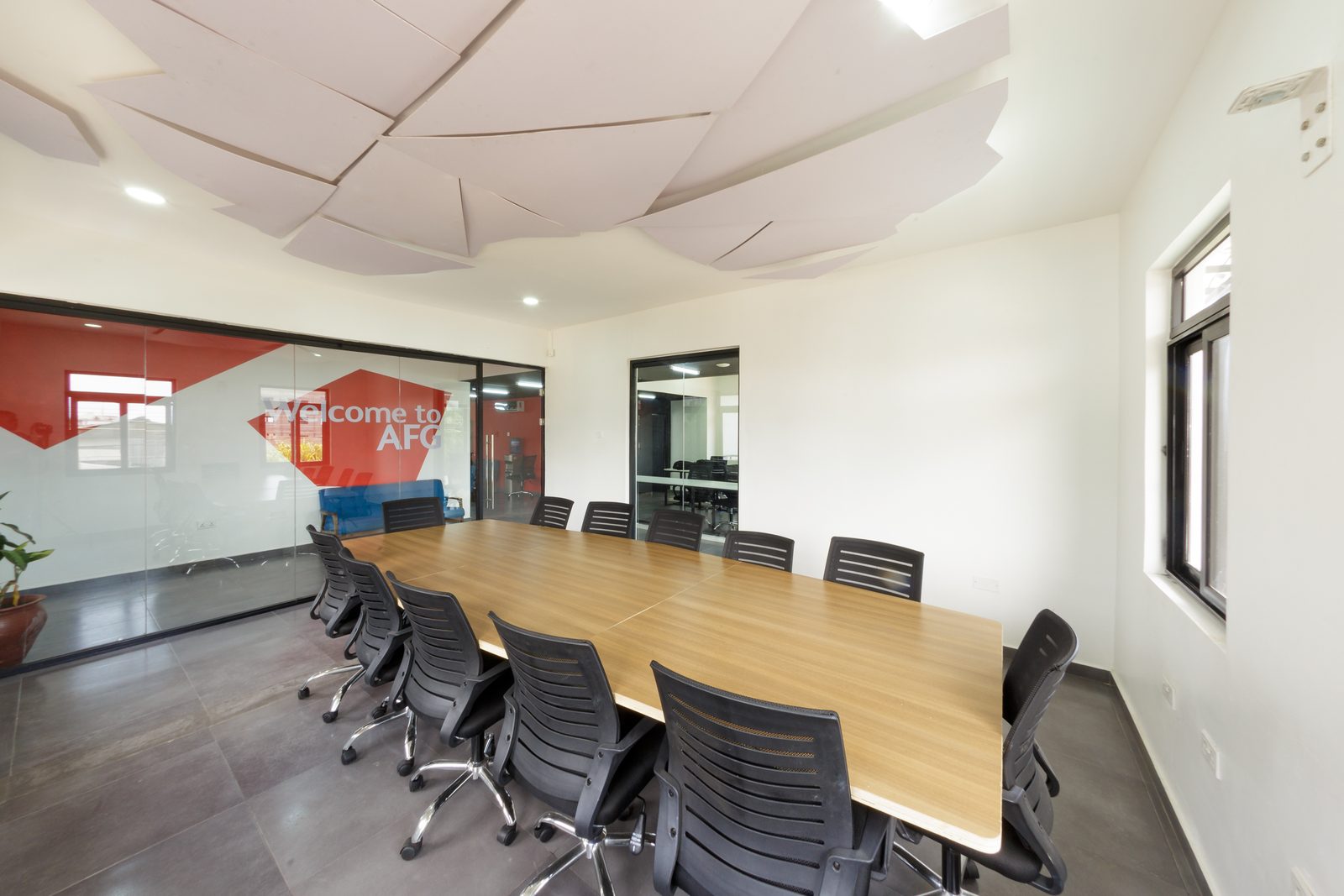 AFG - Down the length of the conference table towards the glazed wall, chairs tucked in under the faceted ceiling.