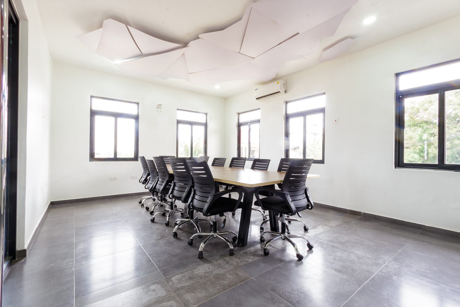 AFG - The long elevation of the conference table, black chairs in two rows beneath the ceiling panels.