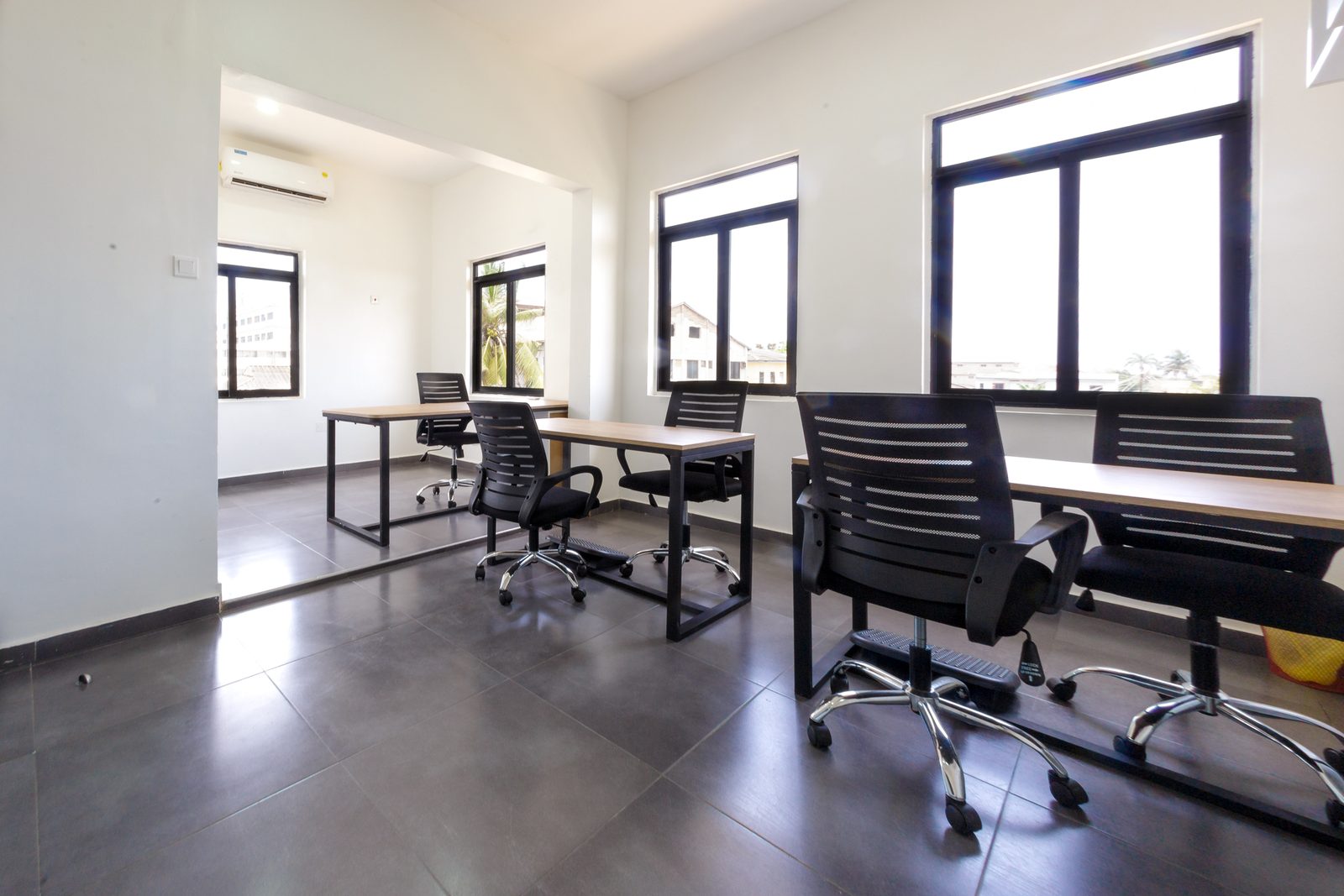 AFG - A management office: two sit-stand desks on black steel frames with plywood tops, black mesh chairs and tall windows.