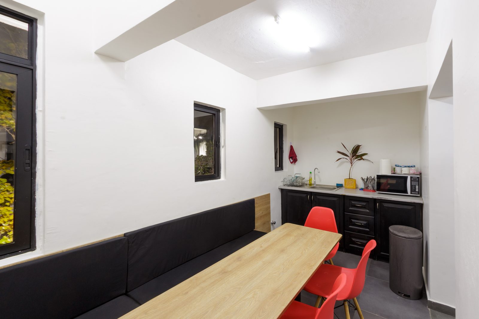 AFG - The dining table from the bench end, red chairs and timber bench seating against a white wall.