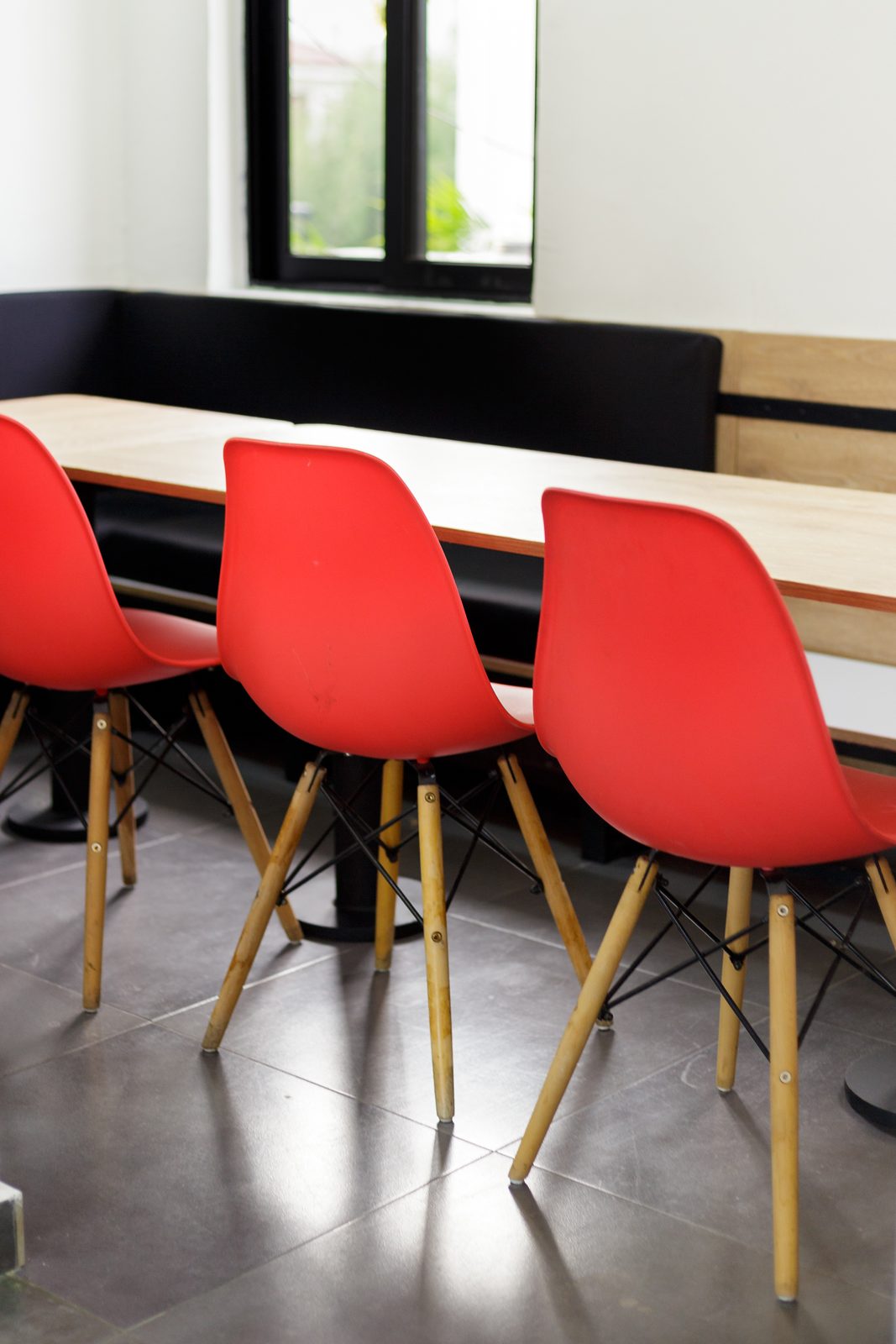 AFG - Portrait detail of the dining corner: black bench seating, plywood table and a red chair by the door.