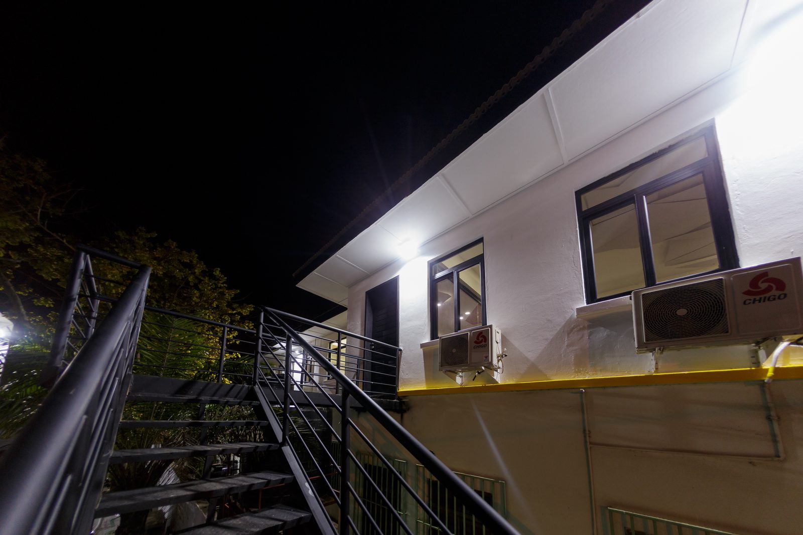 AFG - The night elevation from the yard, floodlights raking across the white walls.