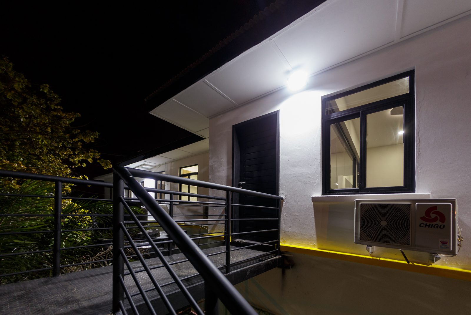 AFG - The corner of the block at night, windows lit and the ochre band reading as a thin line of light.
