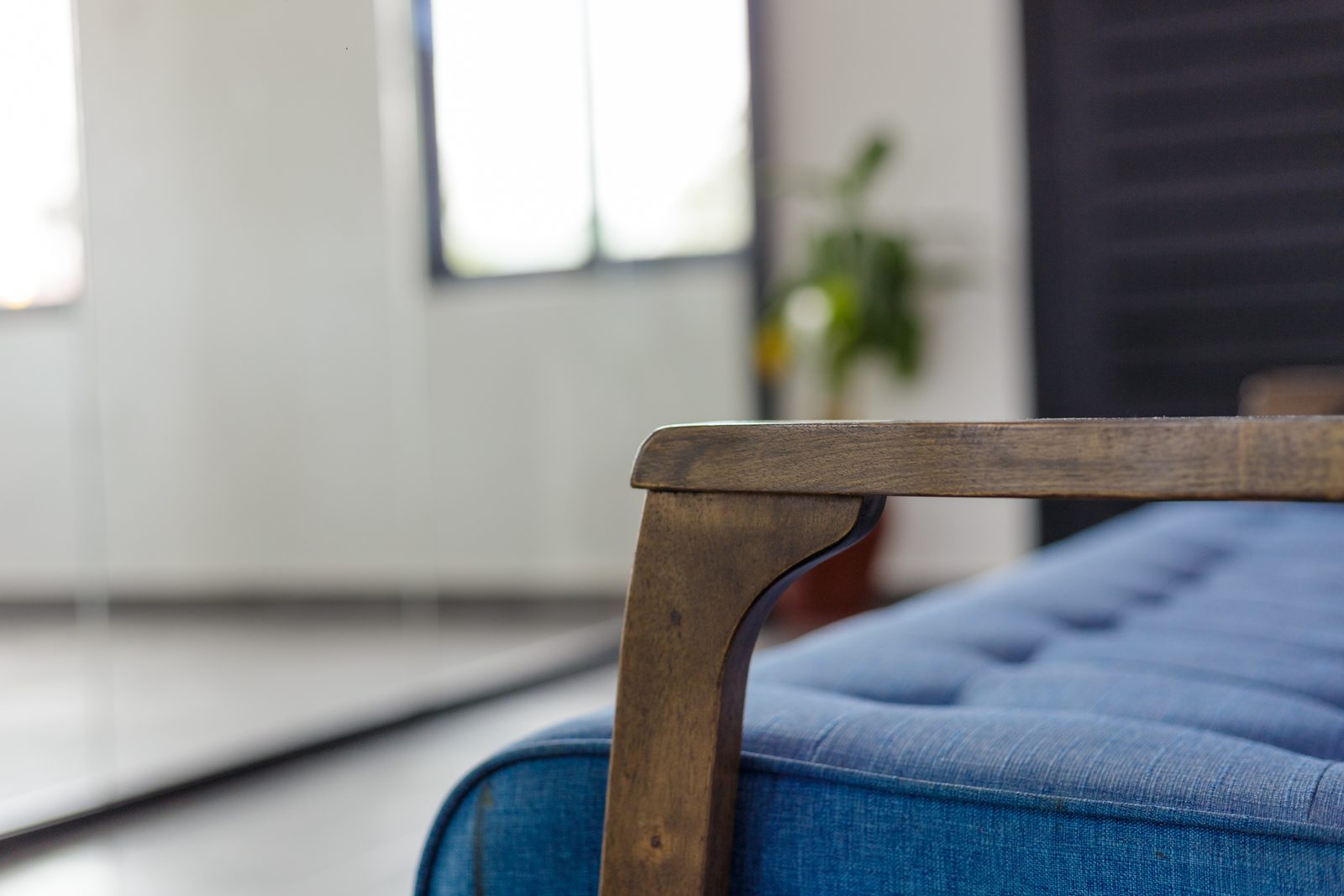 AFG - The corner of a plywood coffee table and the arm of a blue chair, the glazed boardroom wall receding behind.