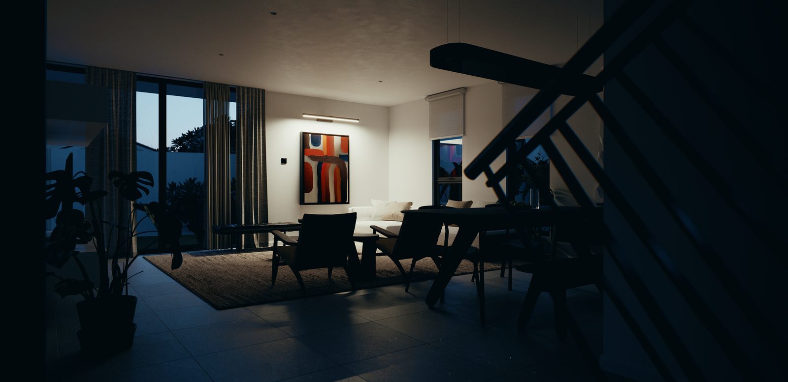 The living and dining volume at dusk, the room lit only by the far lamp and the last light through the glazing, with the stair railing in the foreground.
