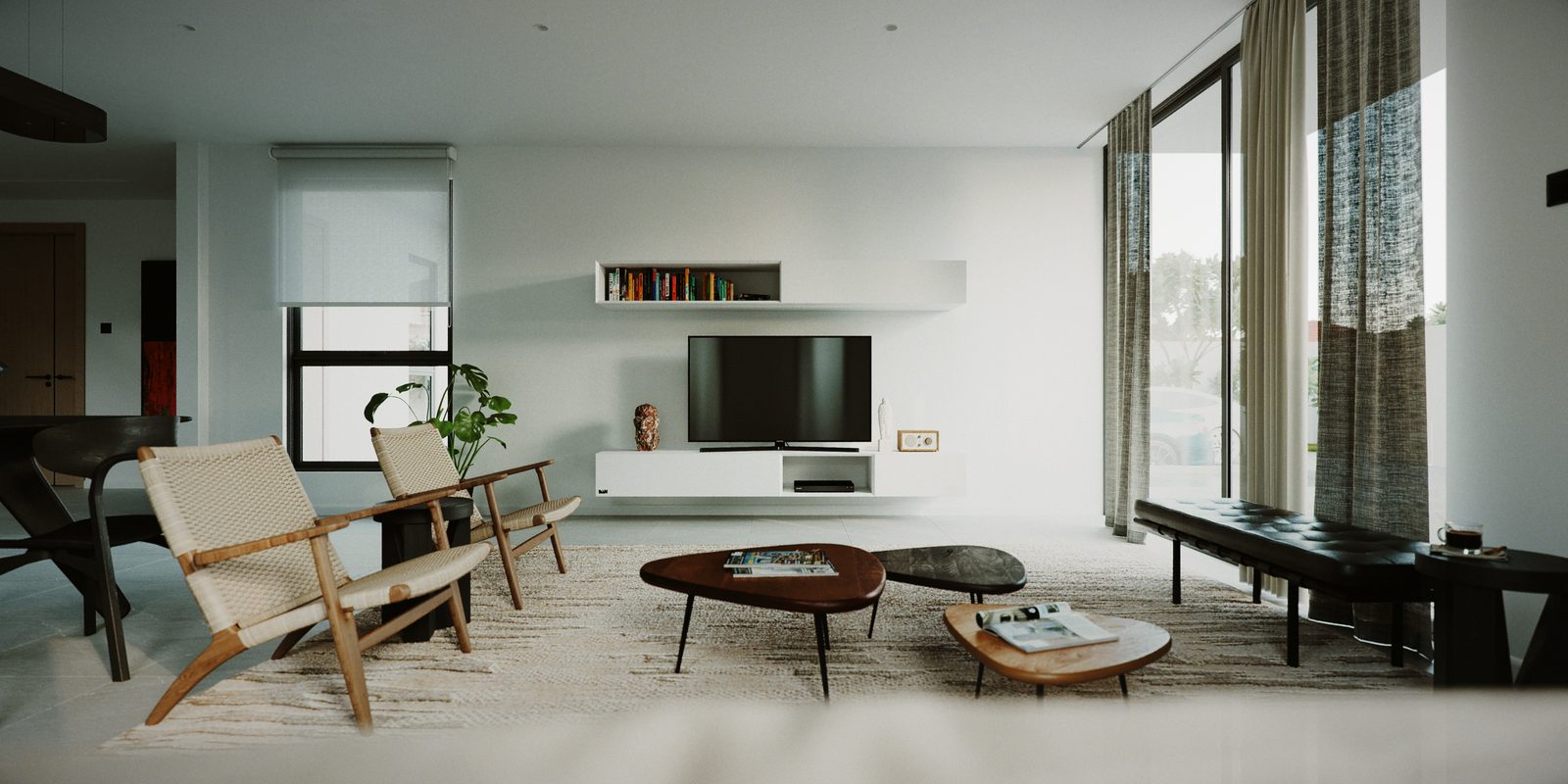 The living room from the window side: lounge chairs, a black bench, low coffee tables and the white media wall with the television and a single floating shelf.