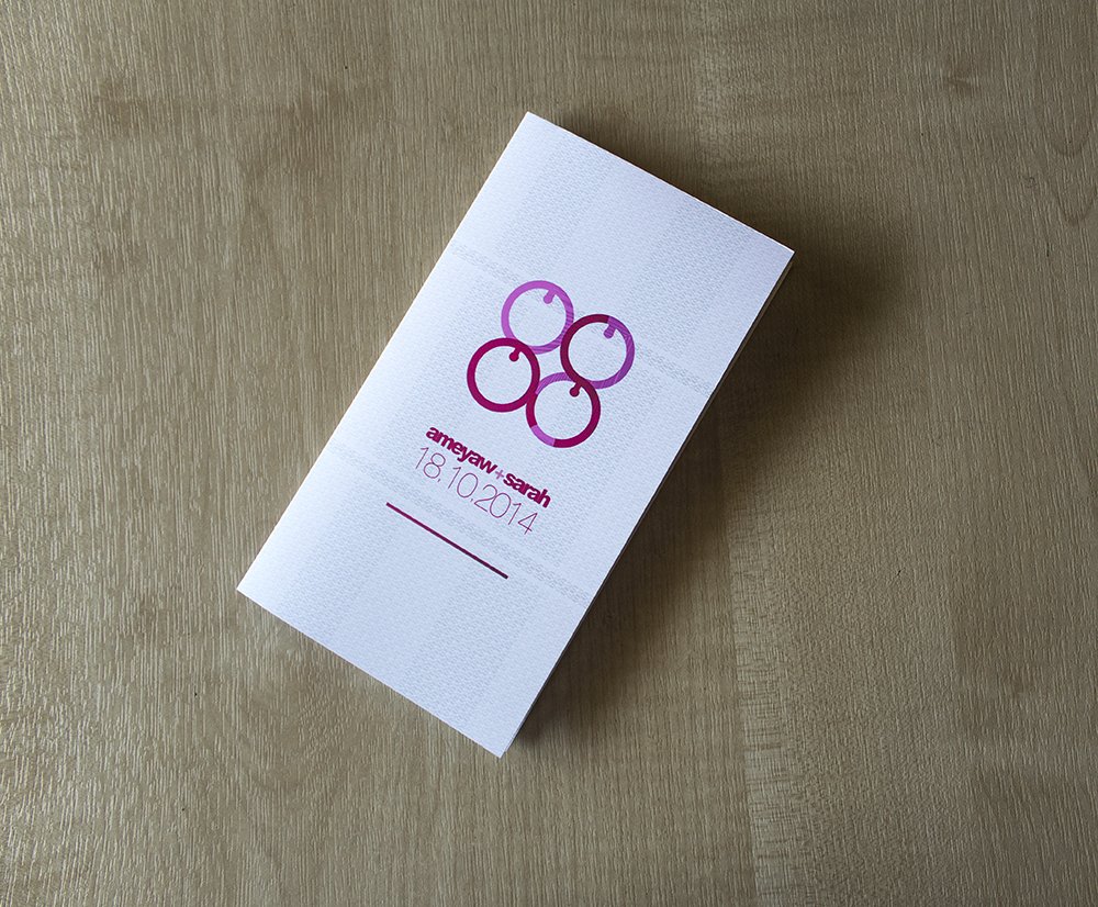 Ameyaw + Sarah printed invitation card on a wooden table, the Me Ware Wo monogram and date in burgundy on white stock
