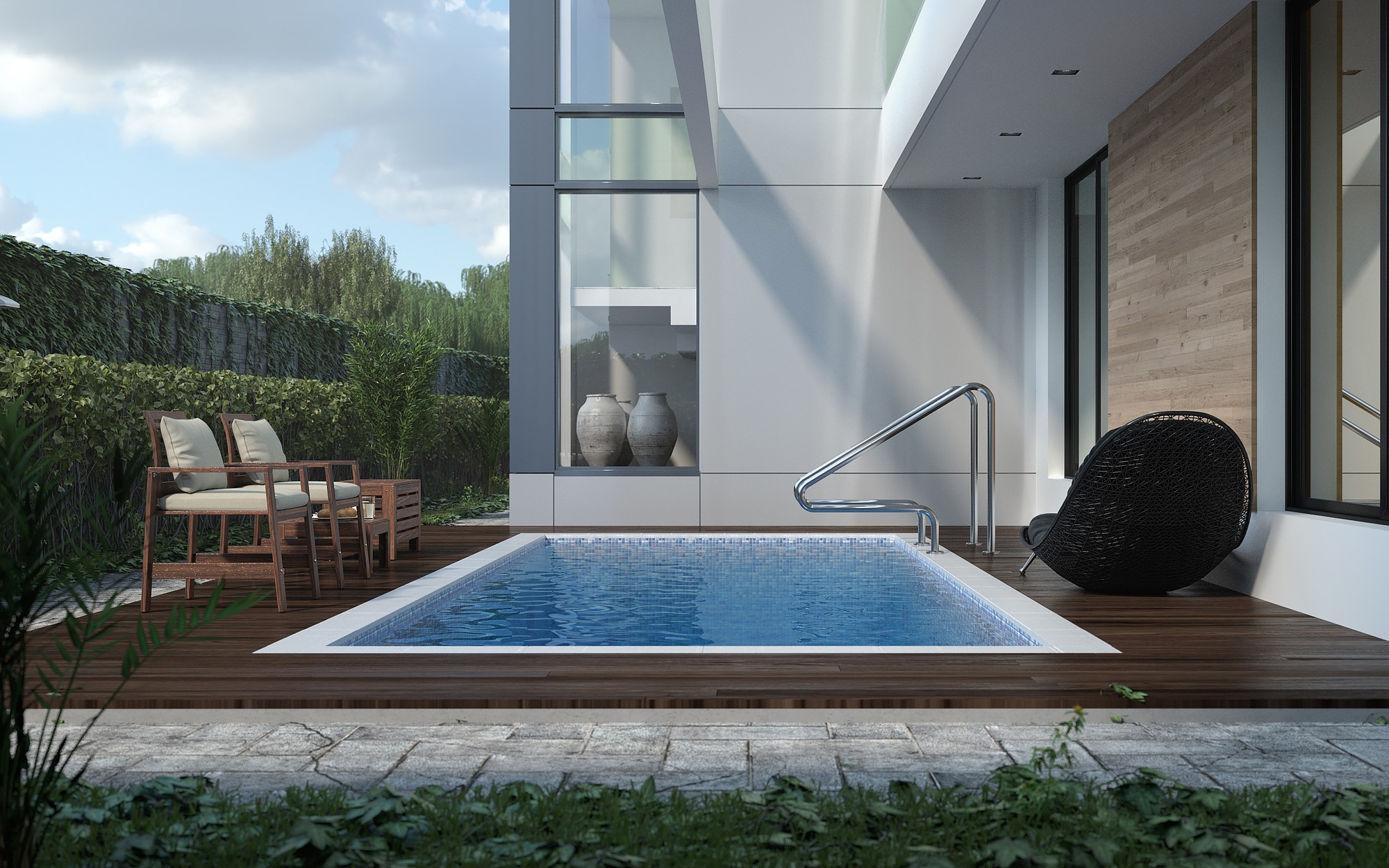 The pool courtyard of a white modernist house: a rectangular plunge pool set into a timber deck between two cushioned deck chairs and a black wicker chair, with a glazed display niche holding two stone urns and a timber-clad wall behind