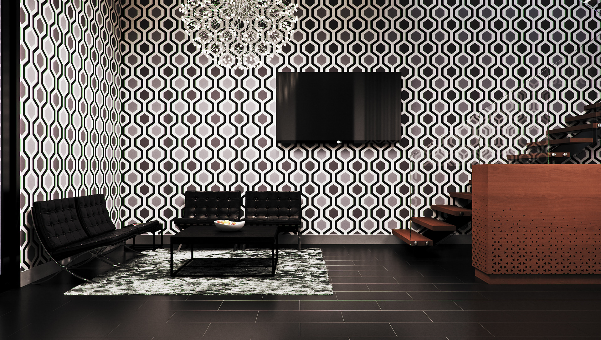 West Cantonments Residence lounge facing the television wall: a flat black screen on hexagonal wallpaper above two tufted black armchairs and the fruit bowl on its table, a crystal chandelier at the top edge and the perforated wood counter at right.