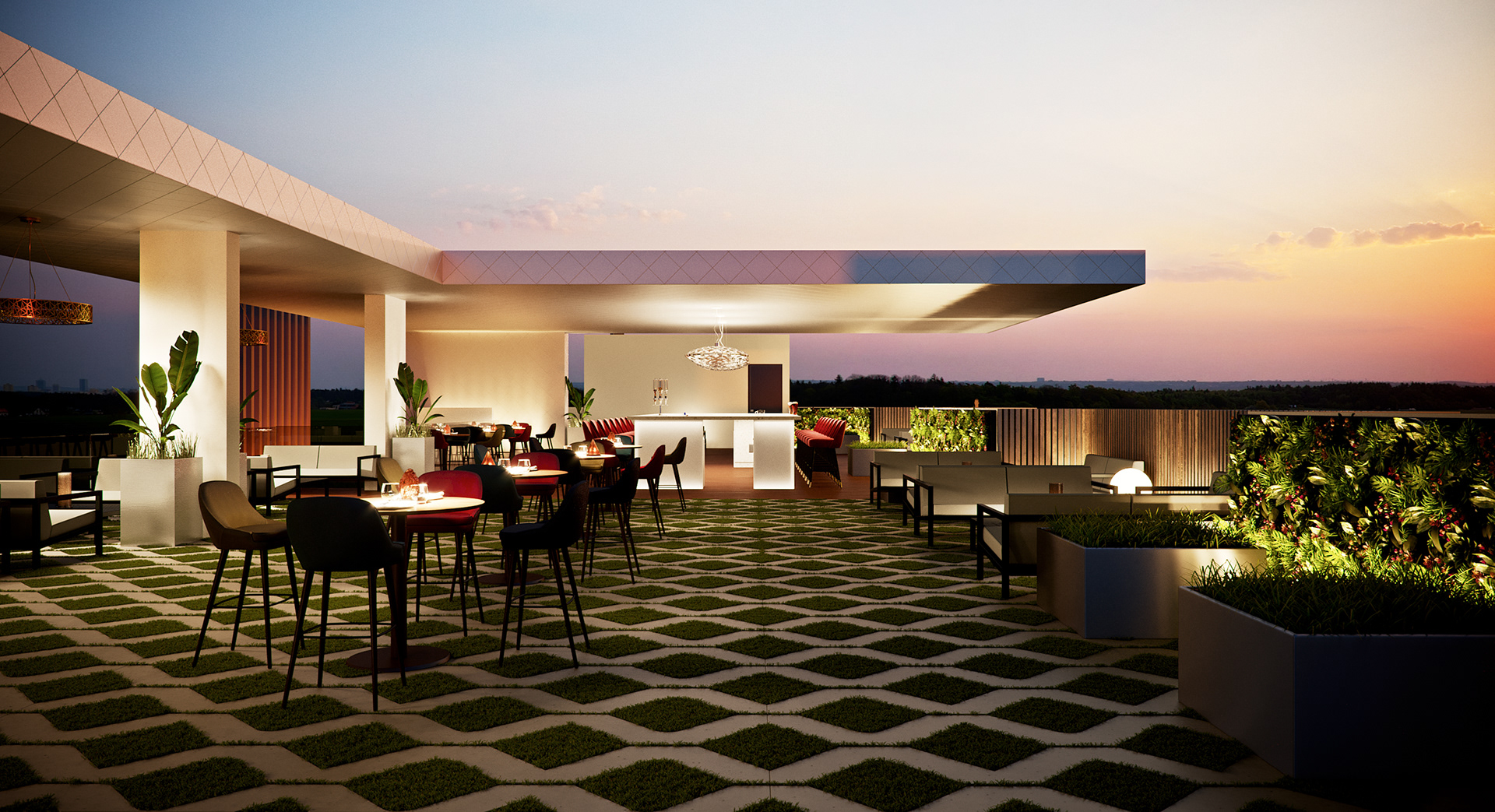 West Cantonments Residence rooftop terrace from the far end looking back at the bar pavilion: grass between diamond concrete pavers, small round high tables with black and red chairs, the illuminated bar under its canopy and an orange sunset horizon.