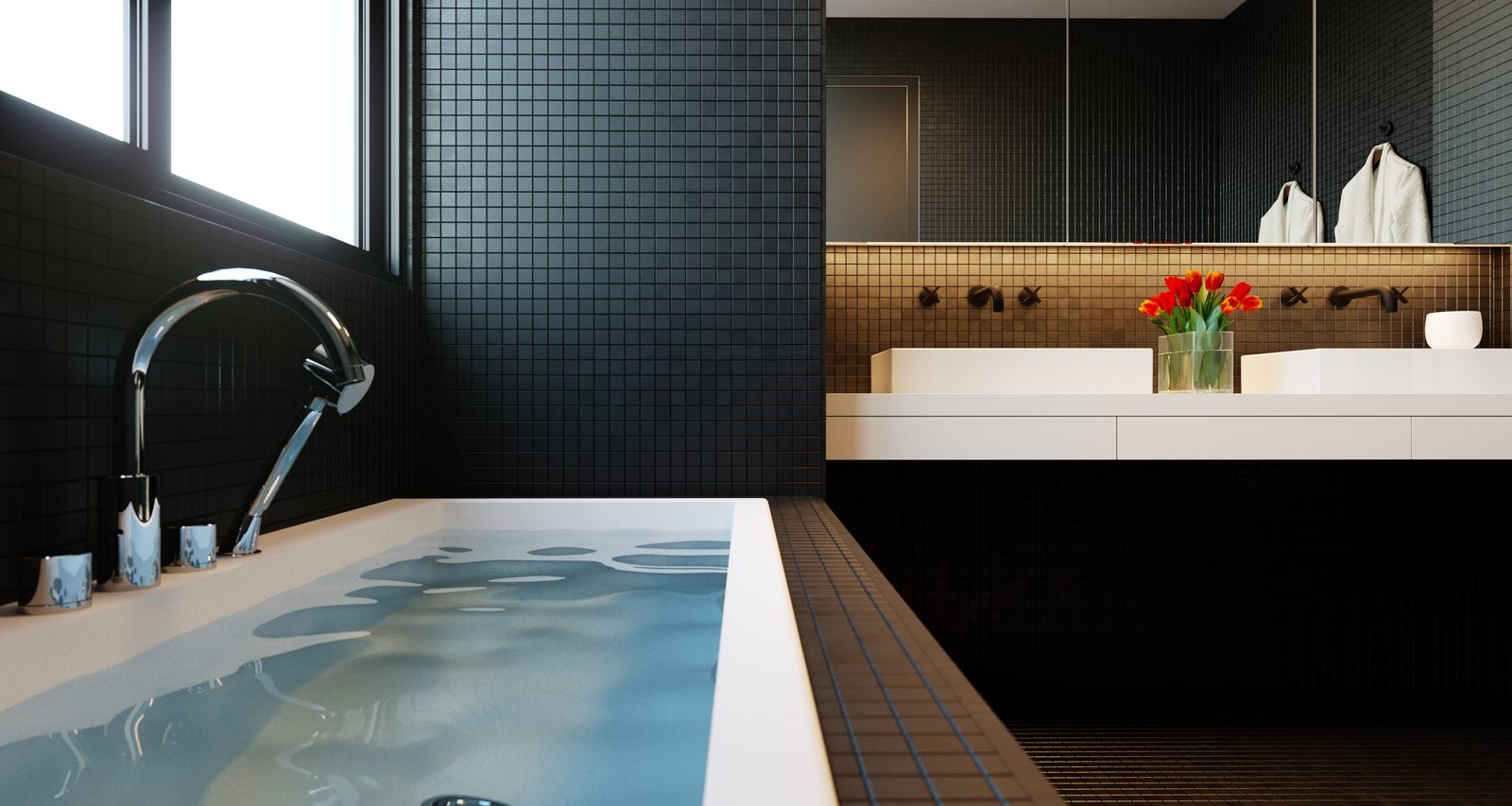 Tower Cascades - Freestanding bathtub with a deck-mounted chrome filler against dark mosaic tiling, the vanity and a vase of red flowers beyond.