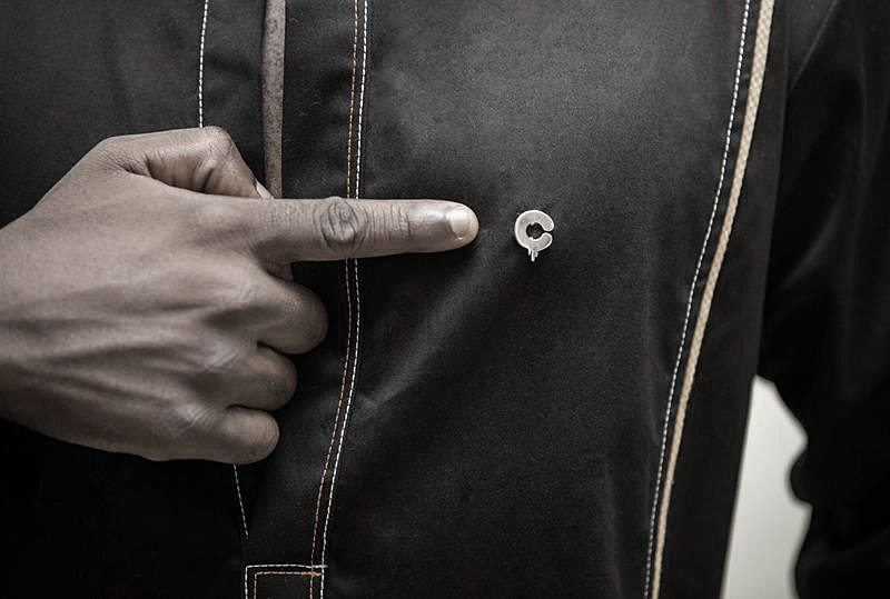Chocolate - the metal C badge pinned to a black jacket: the embossed mark at chest height