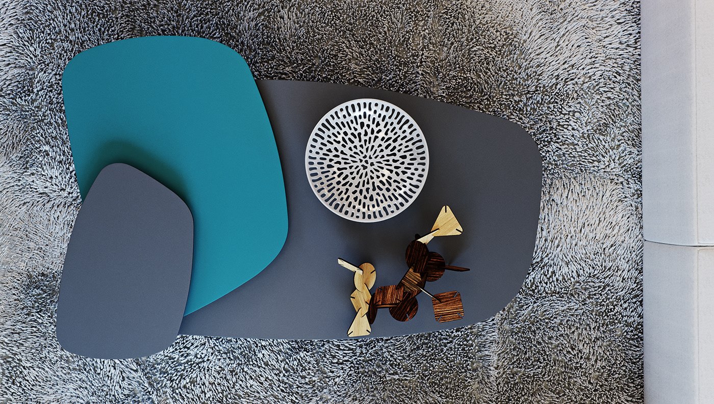 Overhead render looking straight down at a grey shaggy carpet with two flat sculptural shapes in teal and slate grey, a round white openwork tray, and small carved wooden objects placed beside them.