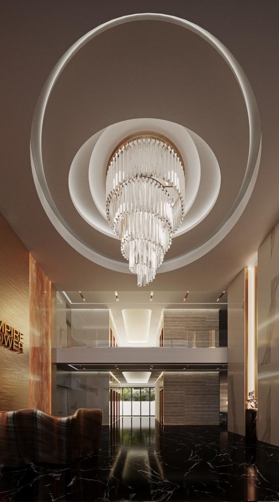 Empire Tower lobby looking up: a tiered crystal chandelier dropped from concentric lit ceiling rings, gilded Empire Tower lettering on a timber wall to the left, and a black marble floor running to the mezzanine corridor.