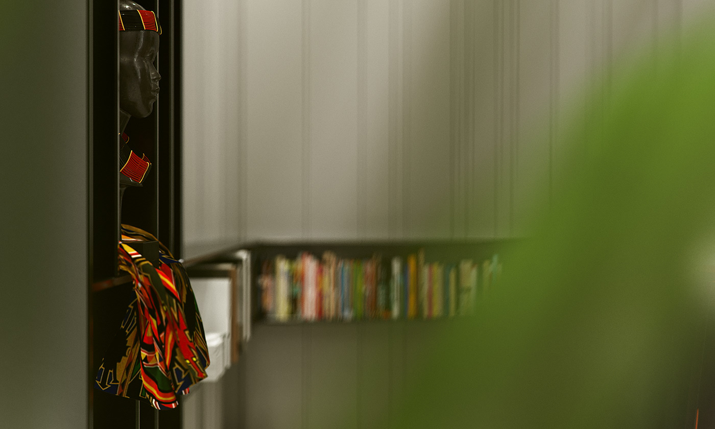 Funko Ridge Residence shelf detail: carved bust in a beaded crown draped with kente cloth on a dark display unit, out-of-focus book ledge beyond.