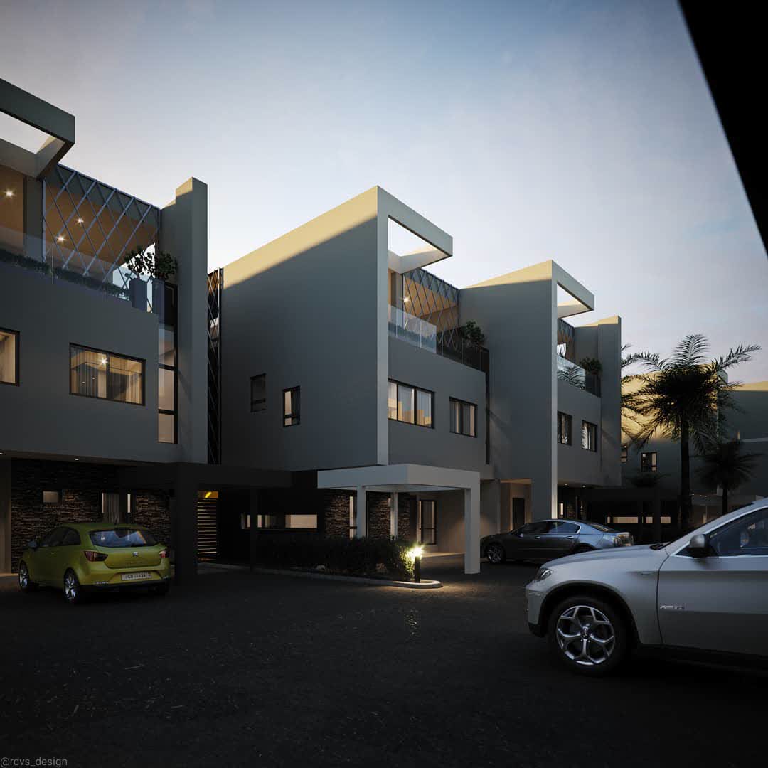 The Hamlet from the parking court at dusk: lit windows and diamond lattice roof screens above stone-clad carports, a lime-green hatchback and a silver SUV on the asphalt, a bollard light glowing in a planted bed, and palms at the right.
