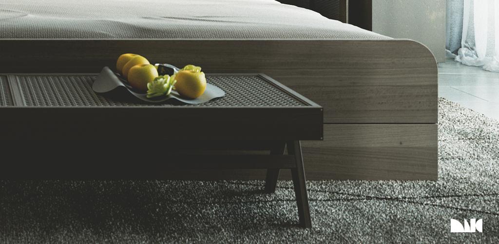 HGG bed foot close-up: a low caned bench carrying a metal tray of citrus against the rounded oak bed base, standing on a grey shag rug by the sheer curtains.