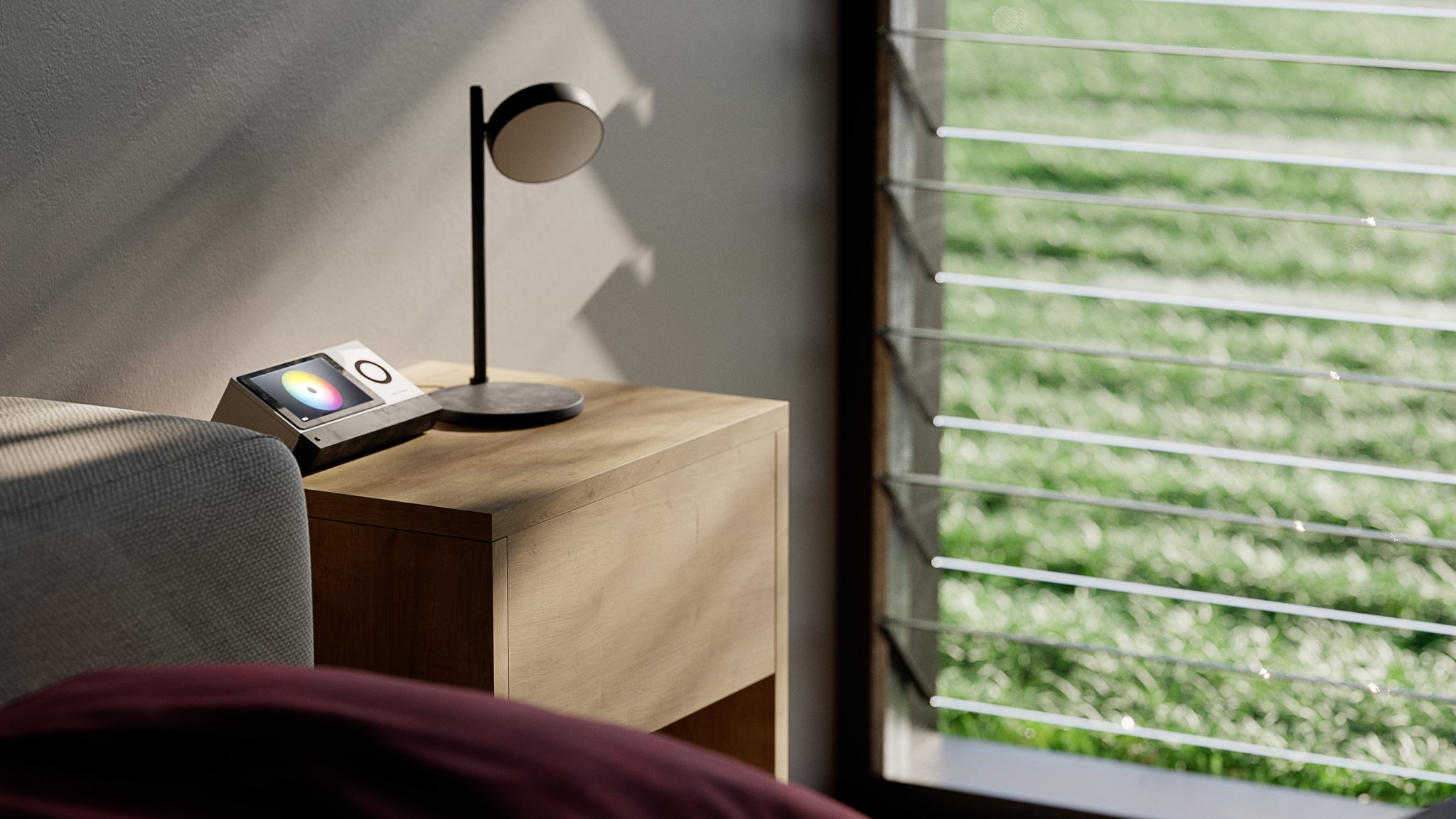 Hola bedroom corner: an oak nightstand by the louvered window onto the lawn, carrying a black disc reading lamp and a smart-home panel lit with a colour wheel, a grey chair and burgundy bedding in the foreground