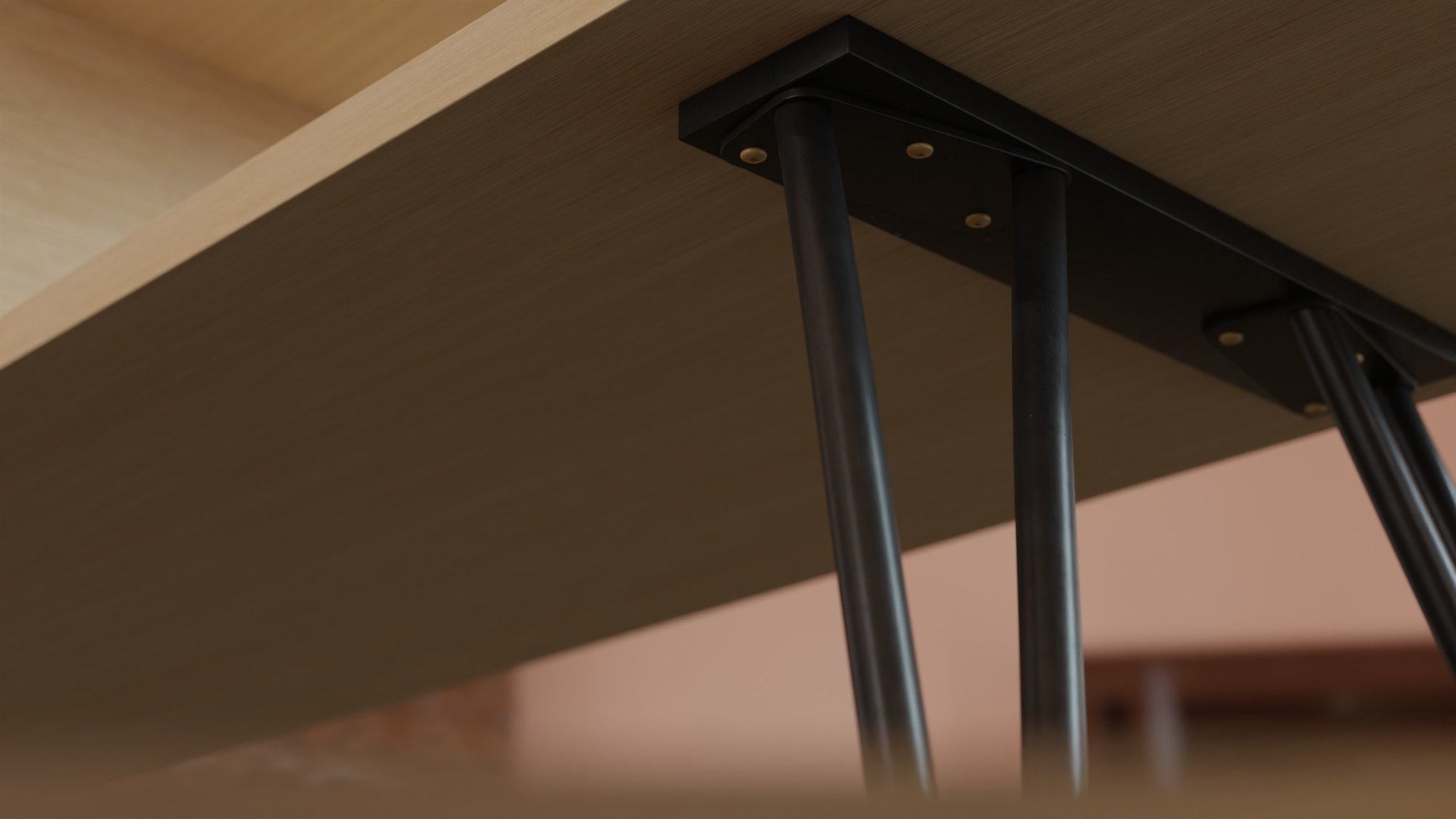 Lamu underframe on the diagonal: the bracket and twin legs read through to a second bracket at the far corner, a pink wall beyond the oak plane.
