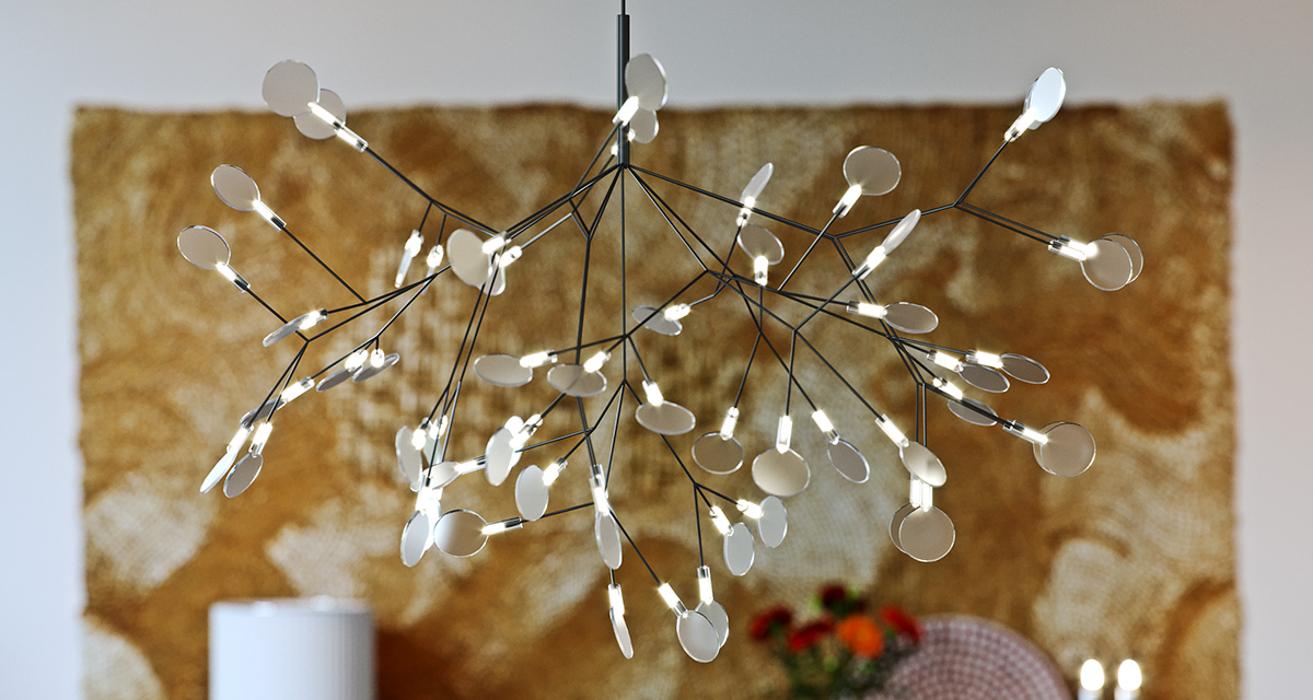 Link Drive Rd. chandelier close up: black rods branching in every direction, each tipped with a small light and a mirrored disc, hung in front of the gold abstract canvas above the laid table.