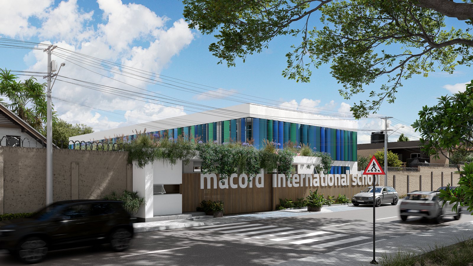 Macord International School seen obliquely from the street: the finned block behind the boundary wall, barbed wire along the plaster wall at the left, utility poles and wires overhead, traffic blurred at both ends.