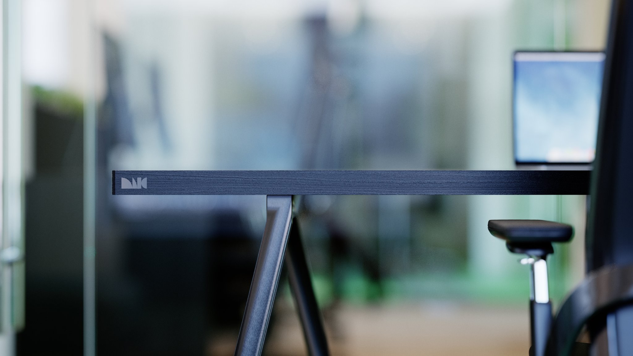 Black-stained desk with trestle legs in a studio, the MIG mark printed on the returned edge of the top.