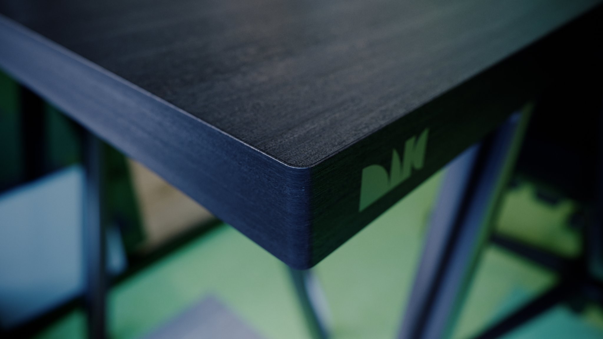 MIG HG-DESK from above in extreme close-up: the rounded corner of the dark wood top, a green-lit logo mark on the end face and the metal legs thrown out of focus below.