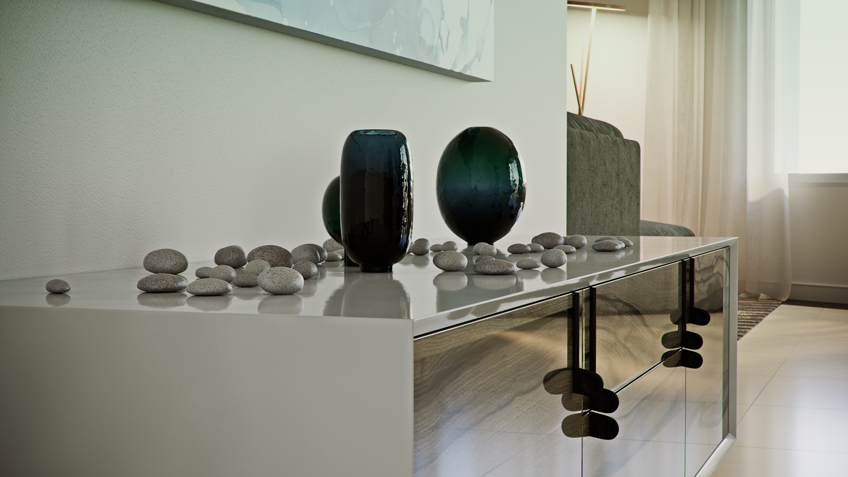 Naadei Villas still life: three dark blue-green glass vessels ringed with smooth grey pebbles on a polished chrome sideboard, the sofa soft in the background.