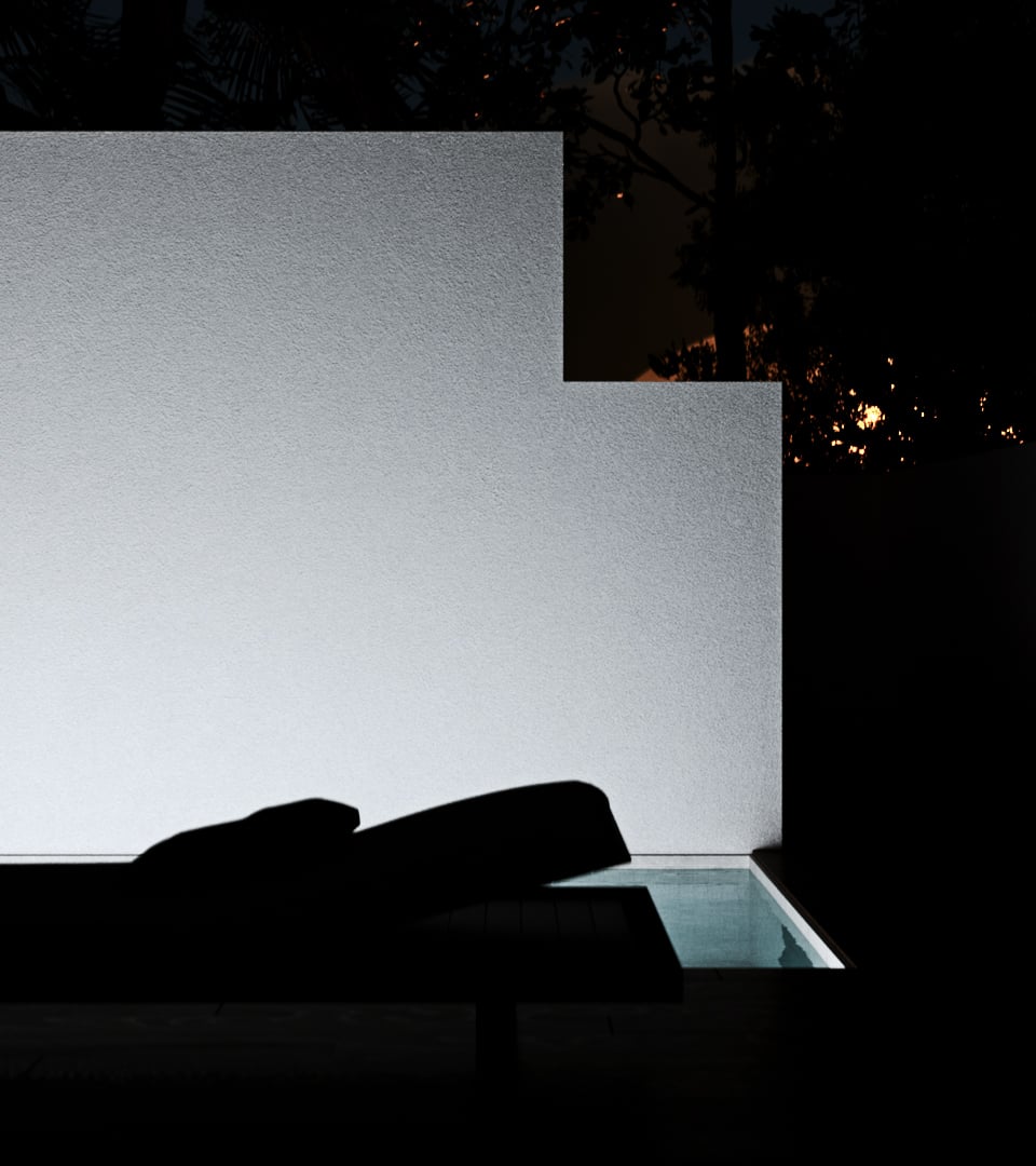 Nyla Court pool at night: the white rendered privacy wall uplit to a soft glow in a stepped L profile, a lounger silhouetted in the foreground and a corner of the water shining pale blue below black trees