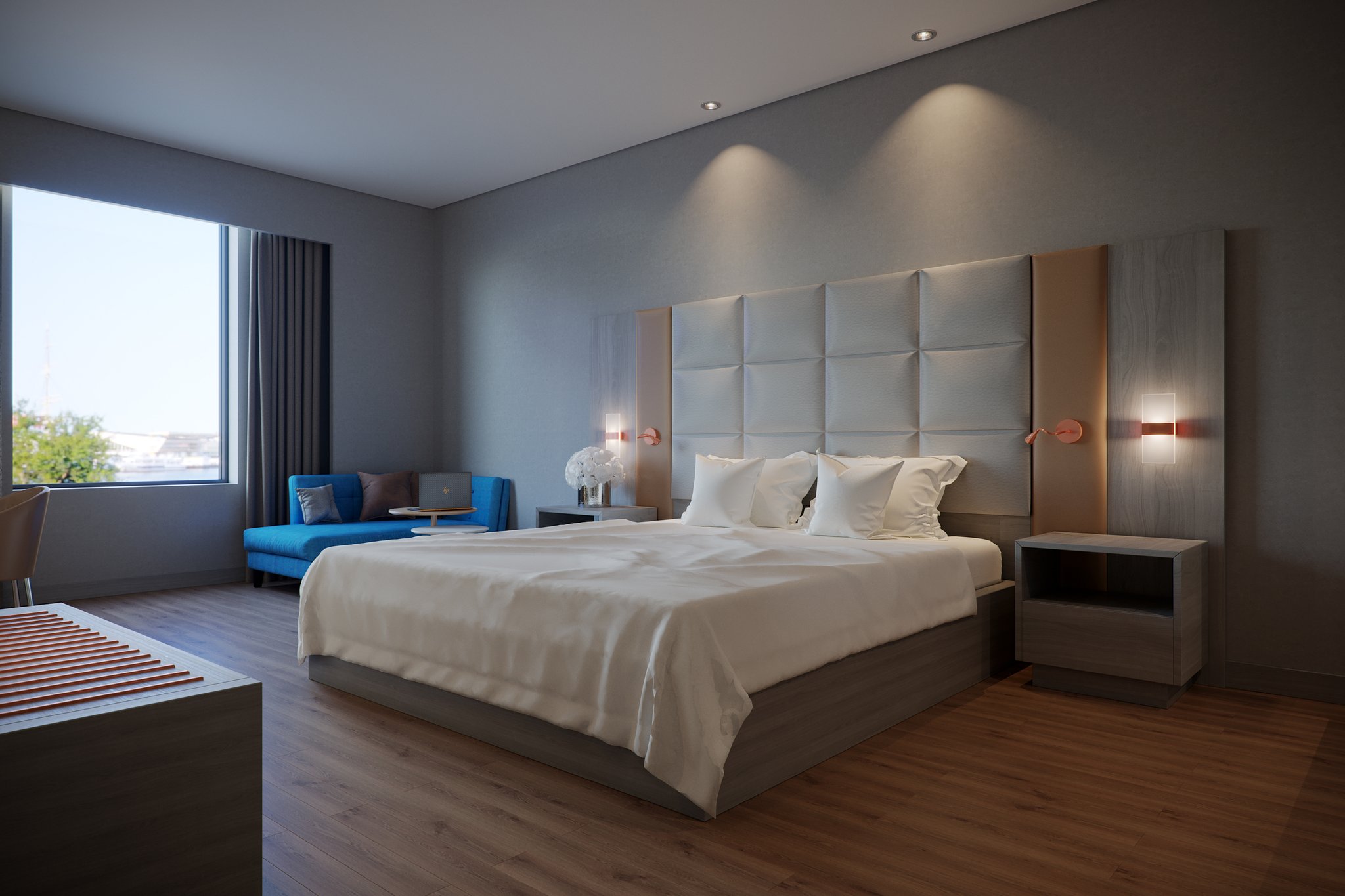Protea Hotel Airport king room from the window end: the bed against a padded square headboard flanked by timber panels, copper sconces and swing-arm reading lights, a blue daybed with a laptop table at the glazing, and a floating nightstand.