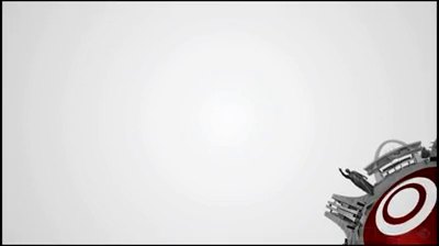 Video still on a bright white-grey field: a flare of light fills most of the frame while the machined gear, with its red concentric target rings, enters from the lower right corner.