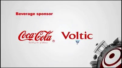 Video still, pale grey sponsor frame: Beverage sponsor in red capitals above the red Coca-Cola script logo and the Voltic wordmark, the silver gear with red rings at the lower right corner.