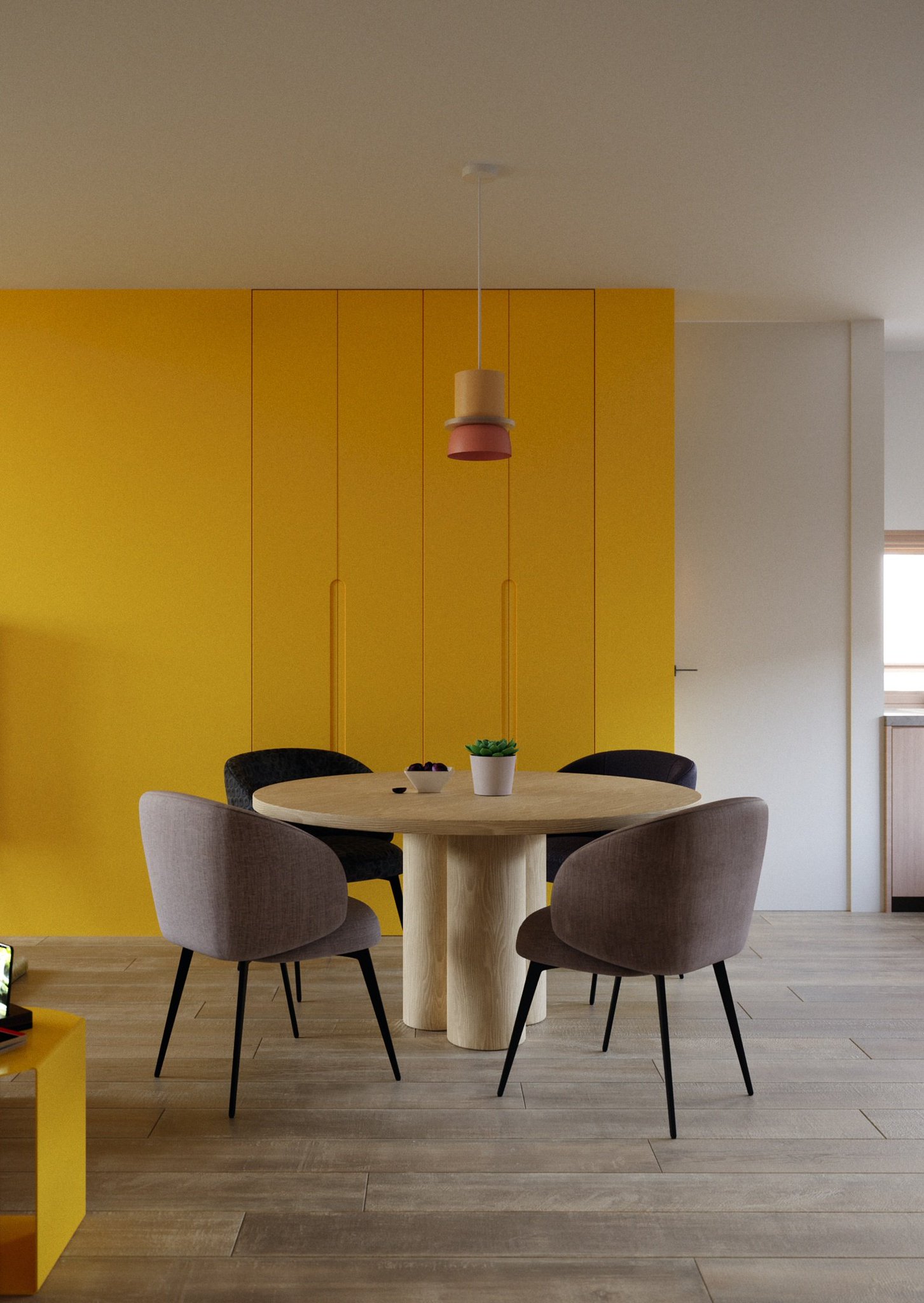 TTD dining table by day: four grey chairs around the oak top with a succulent and a fruit bowl, yellow cabinet doors and a red pendant behind.