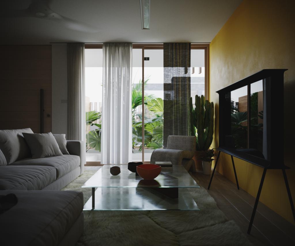 TTD sofa-end view in flat overcast daylight: dim interior, glass coffee table with an orange bowl, grey sofa and black TV cabinet on the yellow wall.